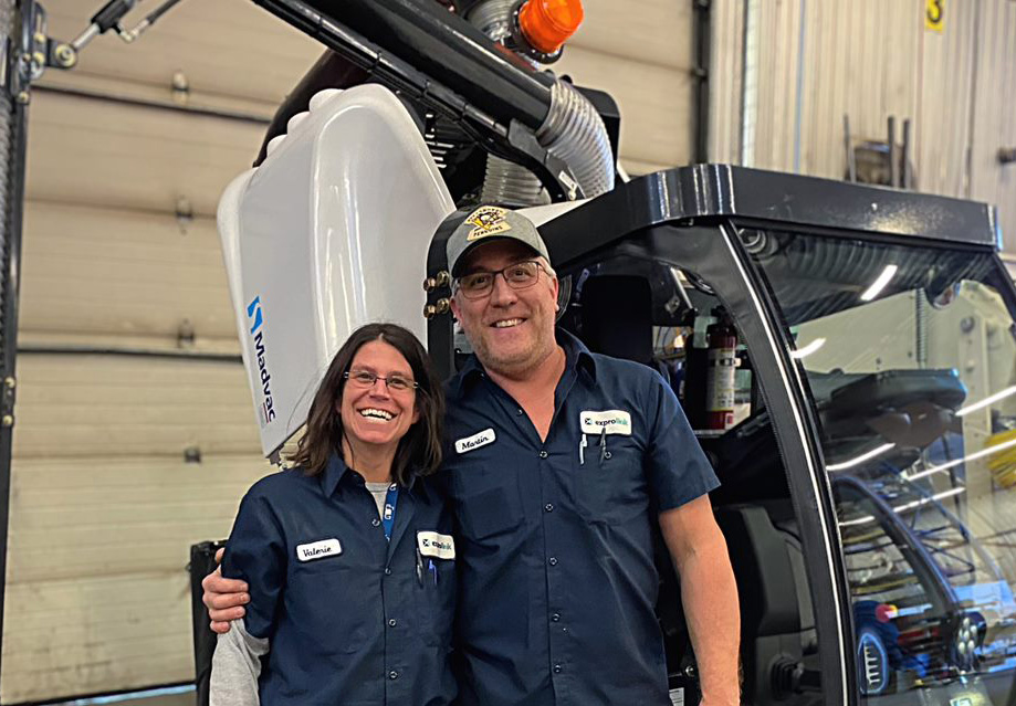 Martin and Valérie, two long-standing Exprolink employees, stand in front of a freshly assembled Madvac vehicle, smiling with camaraderie