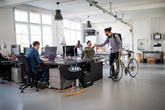 Employees of a software development company greet a colleague who arrives on his bike