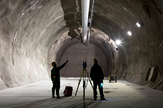 Two employees study the wall of a mining tunnel.