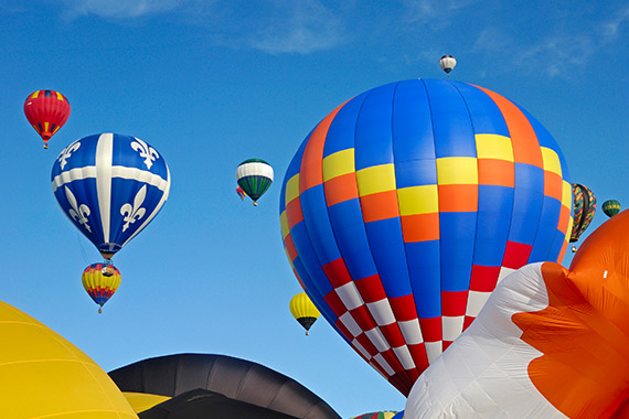 Hot air balloons being inflated and others floating up into a blue sky.