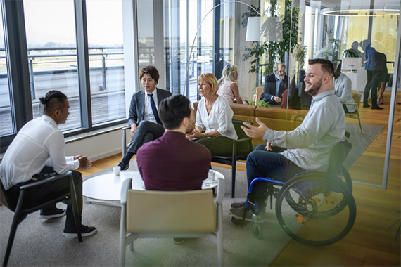 An office meeting between five people from different backgrounds exchanging ideas including one with disability and a women.